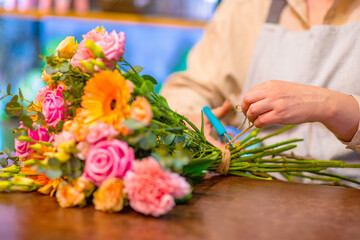 Close-up of a florist's hands tying a bouquet with twine in a flower shop on a wooden table. The master decorator creates a bouquet for a flower arrangement for the celebration