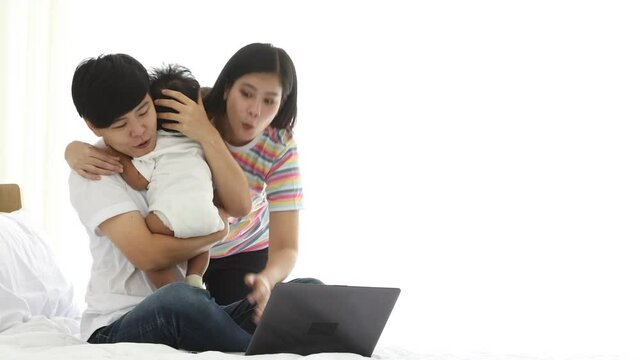 Younger Asian lesbian hug elder female cherish male baby checking laptop online shopping in bedroom on white background with copy space. LGBT family concept