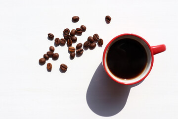 Red cup of coffee and coffee beans on white table background. Hard light, shadow. Summer flat lay minimalist composition. Top view, copy space
