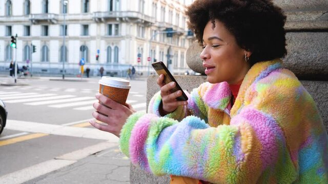 Young diverse unconventional multiethnic woman sitting outdoor drinking coffe-to-go and listening vocal instant message