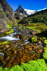 The boulders, crystal clear glacial streams and bright green moss of Stórurð watched by the jagged Dyrfjöll Mountains, Borgarfjörður Eystri, East Fjords, Iceland