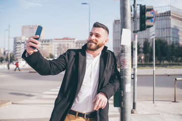 Young bearded caucasian businesslike man outdoor using smartphone selfie