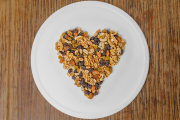 A top view of assorted nuts grouped in the shape of a heart, on a white plate. Almonds, walnuts, hazelnuts, peanuts.