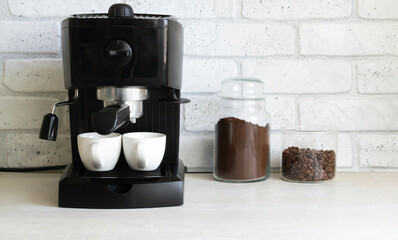 A black coffee machine is on the kitchen table, next to it are two glass jars with ground coffee...