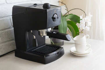 A black coffee machine stands on the kitchen table. Morning traditions. Homemade coffee making concept. Horizontal orientation.