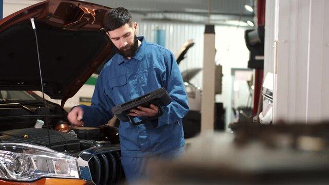 Professional auto mechanic examining car engine, looking under hood