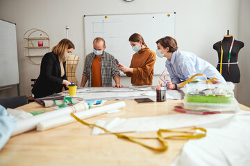 Three people watching a dress designer cutting fabric