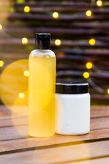 Shampoo and conditioner for hair stand on a woodendark  table on the background lights. There is yellow bokeh in the background and foreground.