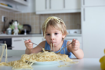 Little blond boy, toddler child, eating spaghetti for lunch and making a mess at home in kitchen