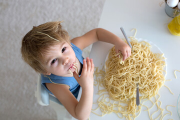 Little blond boy, toddler child, eating spaghetti for lunch and making a mess at home in kitchen