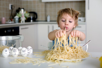 Little blond boy, toddler child, eating spaghetti for lunch and making a mess at home in kitchen