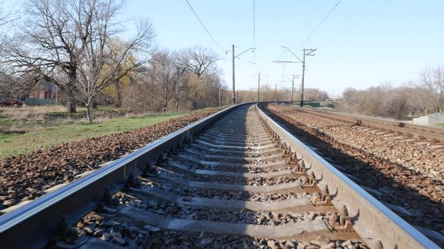 Railroad rails receding into the distance. On the sides are trees without leaves in early spring