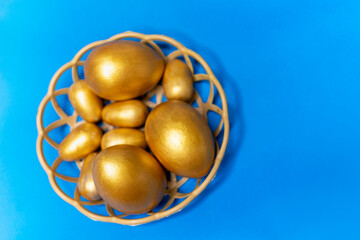 Golden eggs in a basket on a blue background. Happy Easter greeting card. Blue monotone background...