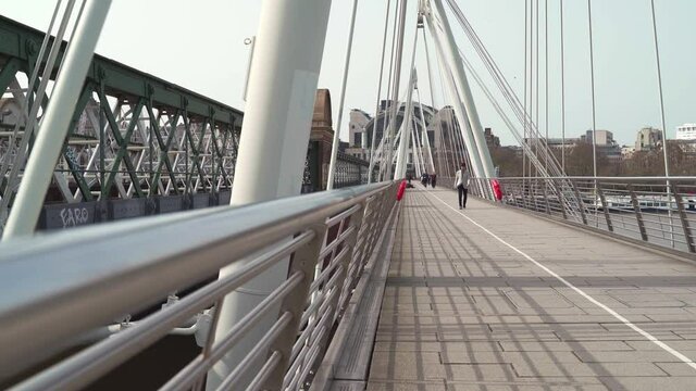 People walking the Hungerford Bridge and Golden Jubilee Bridges on sunny day during Coronavirus pandemic lockdown