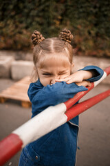 A beautiful girl of about seven years old in a denim jacket stands looking at the camera