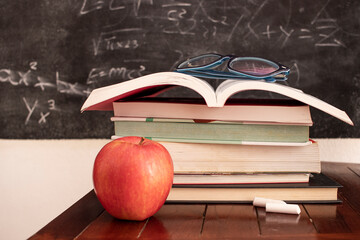 red apple resting next to book stack with chalk blackboard as background