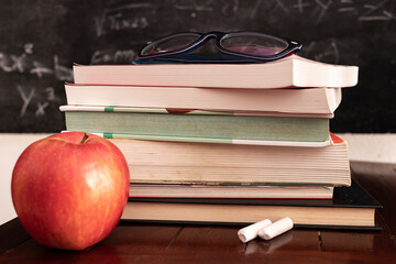 red apple resting next to book stack with chalk blackboard as background