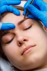 The master plucks out the excess hairs on the eyebrows with tweezers, giving them a shape.
