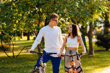 Fototapeta premium Young lovely couple of bicyclists are outdoors looking at each other, feeling happy and having a leisure activity on their bikes.