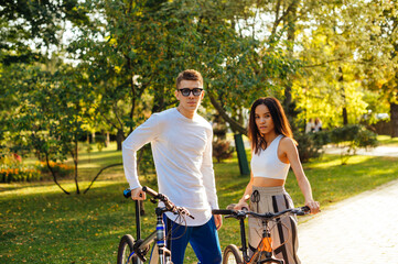 Obraz premium Handsome caucasian man and pretty hispanic woman are standing in the park, holding their bikes, posing for the photo and looking at the camera. Lifestyle, cycling concept.