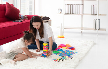 Young girl and her mother enjoy sunny morning playing together. Happy family young mother and cute small kid daughter spend their time together. Mother and her daughter play together in bedroom.