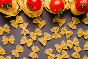 Fettuccine tagliatelle pasta and tomatoes on a gray background. Spaghetti nests. A raw ingredient for traditional Italian cuisine.  Fresh homemade meals or convenience foods. Selective focus.