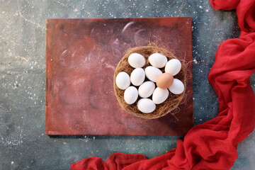 Easter decor concept. White eggs in a wooden wicker basket on a grunge gray background. Red bright material next to the basket. Festive postcard, copy space.