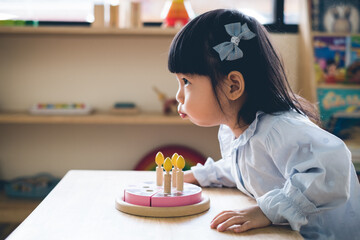 A toddler girl is blowing a toy cake.