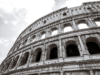 Fototapeta premium Colosseum outside top arches part epic grayscale (black and white) view. Iconic ancient monumental 3-tiered Roman amphitheater, gladiatorial games arena in center of Rome, Italy