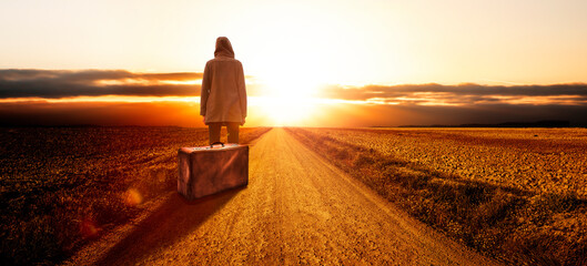 Junge Frau mit einem Koffer bei Sonnenuntergang