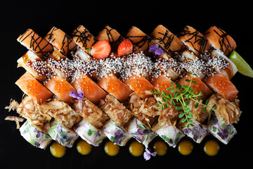 Set of sushi rolls on a dark background with flowers and sauce