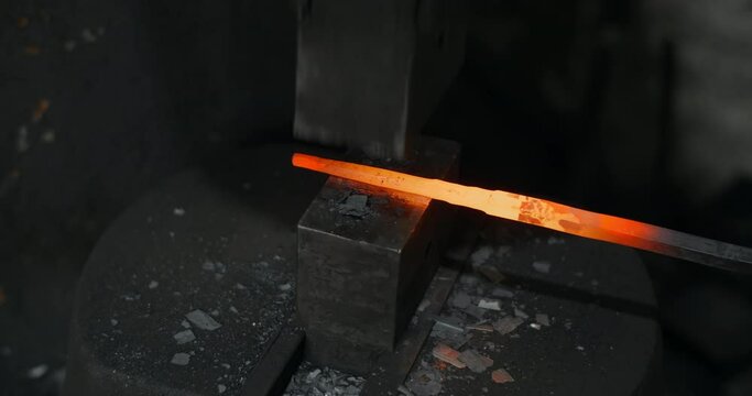 Blacksmith uses a hydraulic hammer to forge hot metal in his workshop, automatic hammer is shaping the red-hot metal, blacksmith craft, forged metal, 4k 60p Prores HQ