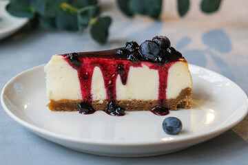 Slice of cheesecake poured blueberry jam decorated fresh blueberries. Tasty cheese pie on plate. 