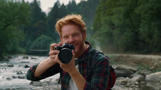 Happy guy with camera standing at river. Photographer taking photos on camera