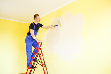 Male specialist paints the wall with paint indoors, repair concept