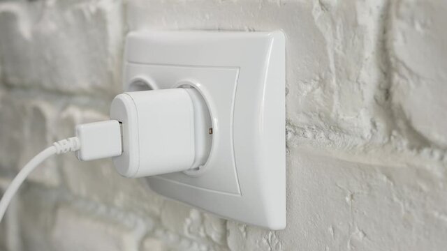 Plugging a Mobile Phone Charger in an Electrical Socket on the Wall. Electronic Charger for a Cellphone Connected on an Outlet.