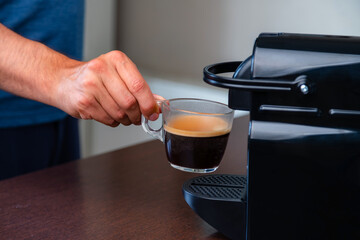 Close up of hand picking up a cup of espresso of capsule coffee machine at home. Concept of coffee break.