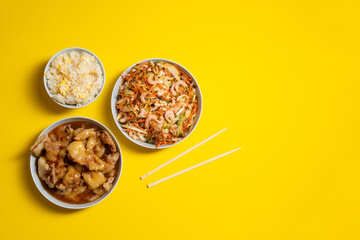 Vibrant plate of shrimp salad, crunchy chicken, bowl of rice with egg and chopsticks on yellow background. Take away food.