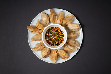 Fried gyoza style dumplings in a plate with spicy soy sauce on black background. Take away asian food.