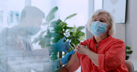 Old caucasian senior woman having doctor appointment in laboratory office. Young doctor injecting...