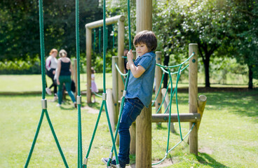 Active kid holding robe in playground, Child enjoying outdoors activity in a climbing adventure park on sunny day summer, Cuteyoung boy having fun on a public playground.