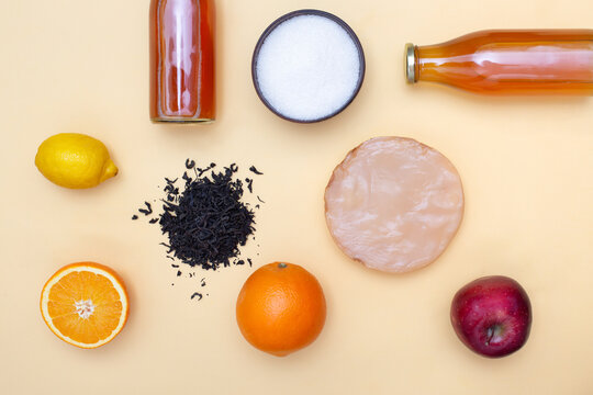 Two Bottles Of Kombucha Tea, Scoby And Fruits For Additional Flavors On Yellow Pastel Background. Orange, Lemon, Apple. Healthy Fermented Drink. Flatlay.