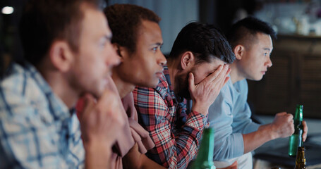 Fototapeta premium Multi-ethnic joyful friends watching football competition matches on TV enjoying sport channel gathering together communicating in the evening.