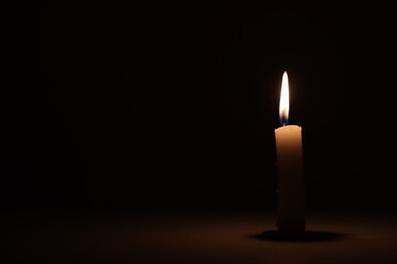 A candle burning alone in a dark room. 