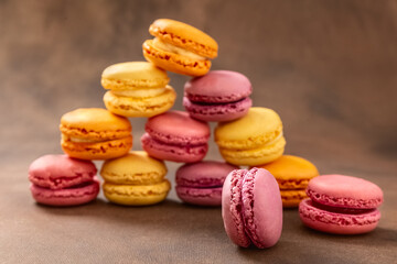 Fototapeta na wymiar Macaroons. Multicolored Macaroons on a brown background. Pyramid. Pink, yellow and red Macaroons. French cake. Place for your text. High quality photo