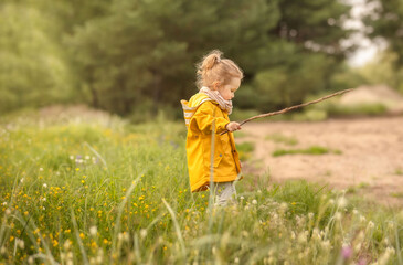 2 years old girl walking in the park. Little girl in yellow raincoat playing in the forest.