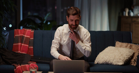 Young caucasian smiling man returning home opening laptop to play favorite video game loosening...