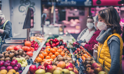 woman in yellow vest and mask buying Mediterranean fruits and vegetables in a traditional market. healthy food and Mediterranean diet of proximity.