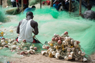 Escena con un hombre reparando redes de pesca en la playa de Sanyang en la costa de Gambia