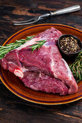 Raw lamb mutton thigh or leg with rosemary and thyme in rustic plate. Dark wooden background. Top view